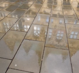 Nach dem Regen spiegelt sich die Fassade in den Steinplatten